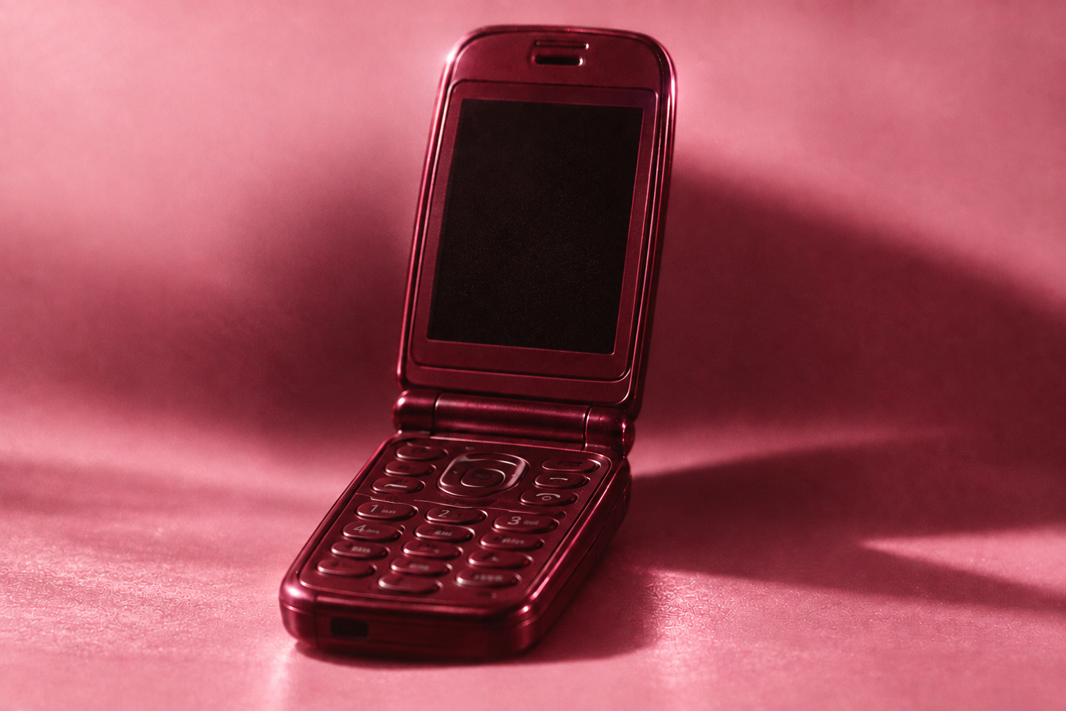 Open burgundy flip phone on a softly lit baby-pink surface